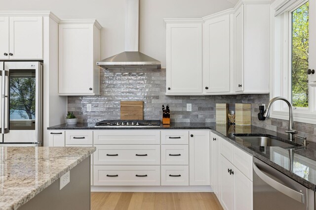 1929 Fagerness Point Rd, Orono, MN 55391 - kitchen with stainless steel appliances, wall chimney range hood, a sink, dark stone counters, and white cabinets