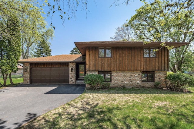 split level home featuring a front yard, brick siding, a garage, and aphalt driveway