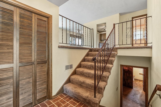 stairway with brick floor, baseboards, and visible vents