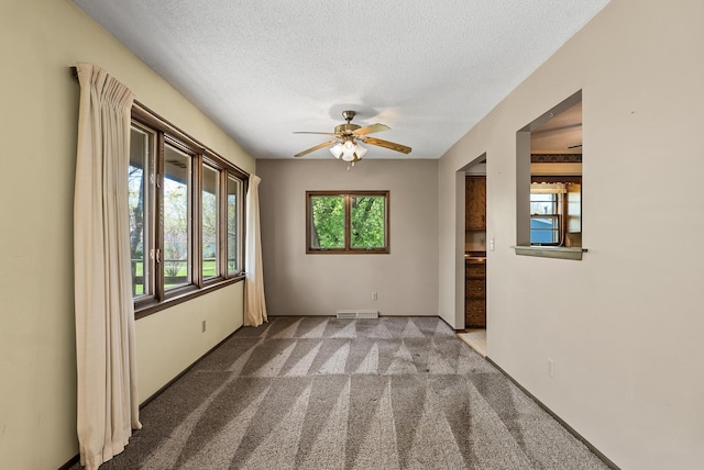carpeted empty room featuring a textured ceiling, baseboards, a ceiling fan, and visible vents