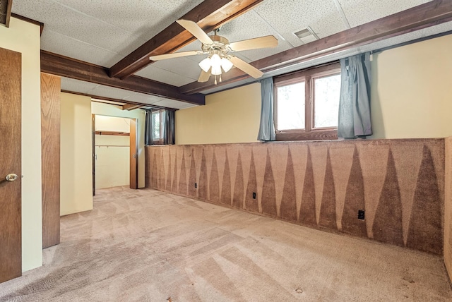 carpeted empty room featuring beamed ceiling, a ceiling fan, and visible vents