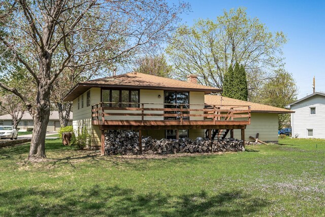 rear view of house featuring a chimney, a yard, a wooden deck, and roof with shingles