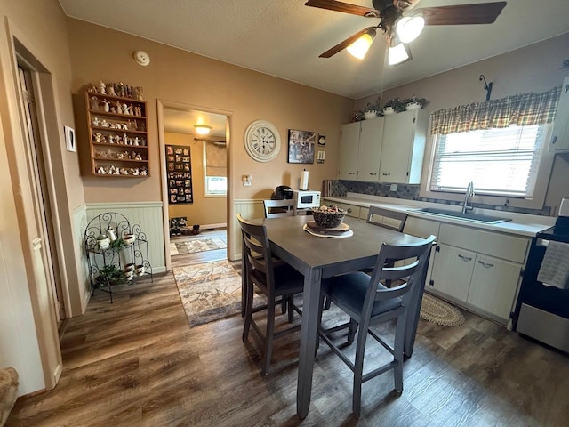 dining room with a wainscoted wall, ceiling fan, and dark wood-type flooring