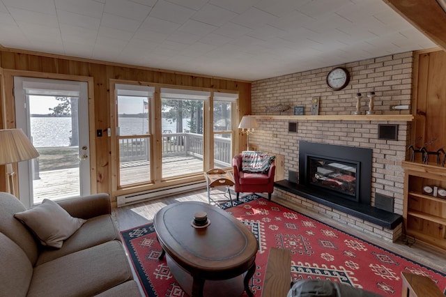 living area featuring a baseboard radiator, wood finished floors, wood walls, and a brick fireplace