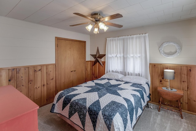 carpeted bedroom featuring wooden walls, a ceiling fan, and a wainscoted wall