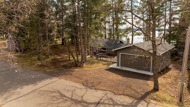 view of front facade featuring driveway, a garage, a shingled roof, and a chimney