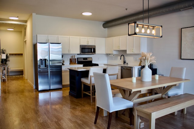 kitchen with a sink, stainless steel appliances, white cabinetry, decorative backsplash, and a kitchen island