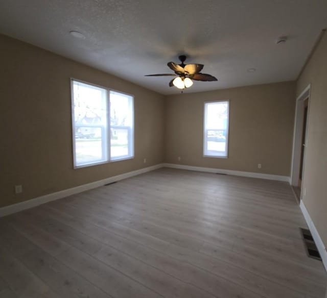 empty room with baseboards, visible vents, a ceiling fan, and light wood-style floors