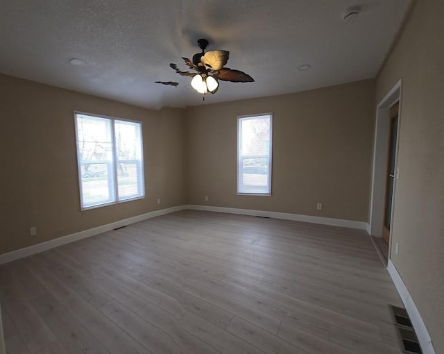 unfurnished room with light wood-style floors, ceiling fan, visible vents, baseboards, and a textured ceiling