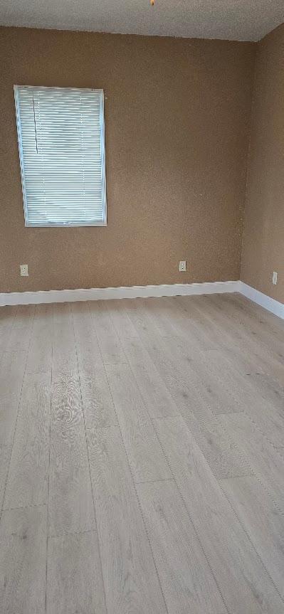 spare room featuring baseboards and light wood-type flooring