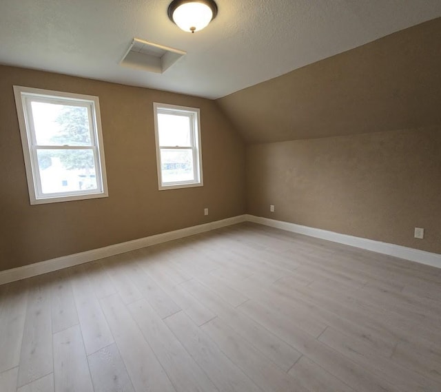 bonus room featuring lofted ceiling, a textured ceiling, wood finished floors, and baseboards