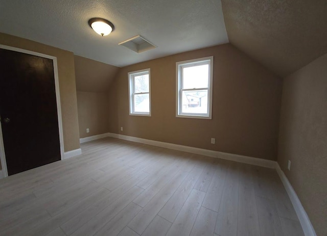 additional living space featuring lofted ceiling, a textured ceiling, and baseboards