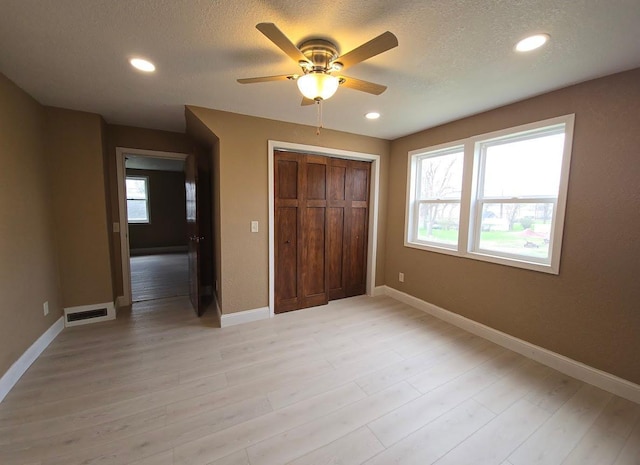 unfurnished bedroom featuring light wood-style floors, a closet, baseboards, visible vents, and a textured ceiling