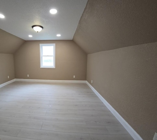 bonus room with a textured ceiling, baseboards, lofted ceiling, and light wood-type flooring