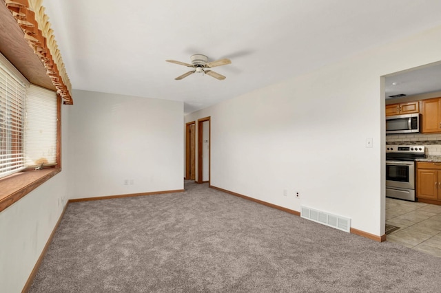 spare room featuring ceiling fan, light carpet, and baseboards