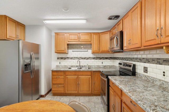 kitchen featuring appliances with stainless steel finishes, a sink, tasteful backsplash, light stone countertops, and brown cabinetry