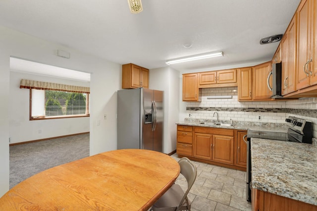 kitchen featuring stainless steel appliances, decorative backsplash, a sink, light stone counters, and brown cabinetry