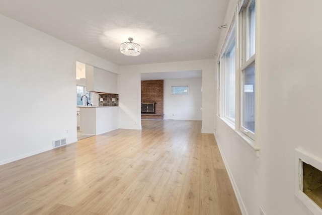 6715 Bloomington Ave, Richfield, MN 55423 - unfurnished living room featuring a notable chandelier, light wood-style floors, a brick fireplace, baseboards, and visible vents
