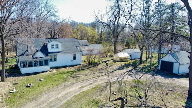 exterior space featuring a detached garage, dirt driveway, a shingled roof, and an outbuilding