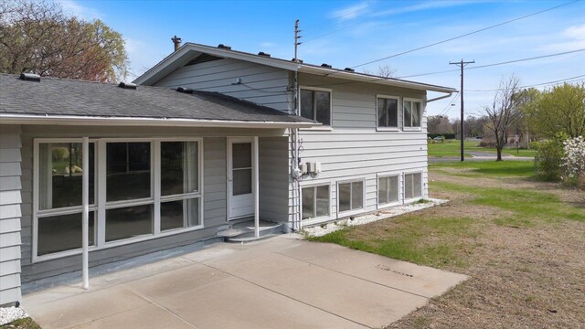 back of house featuring a lawn, a shingled roof, and a patio area