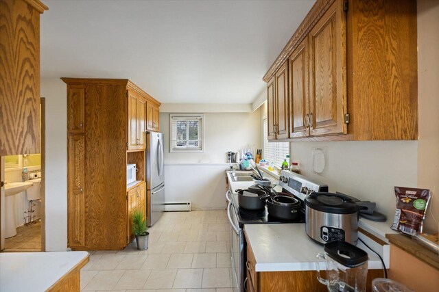 kitchen featuring brown cabinetry, a sink, baseboard heating, and stainless steel appliances