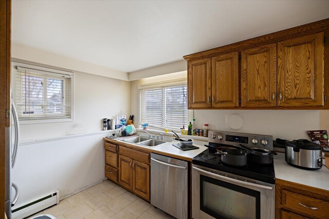 kitchen with appliances with stainless steel finishes, baseboard heating, brown cabinets, a sink, and light countertops