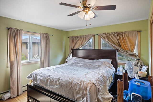 bedroom with ceiling fan, a baseboard heating unit, and wood finished floors