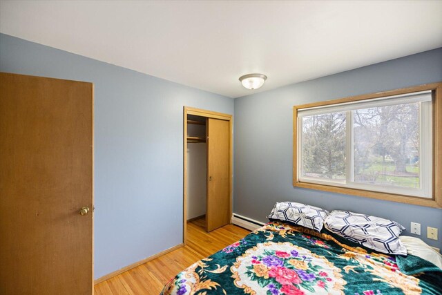bedroom featuring a closet, baseboards, baseboard heating, and light wood-type flooring