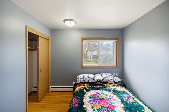 bedroom with a closet, light wood-style flooring, and a baseboard heating unit