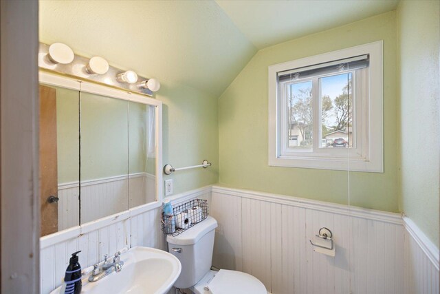 half bath with a sink, wainscoting, vaulted ceiling, and toilet