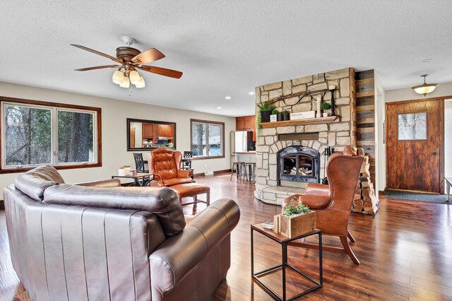 living room with ceiling fan, a fireplace, dark wood-style flooring, and a textured ceiling