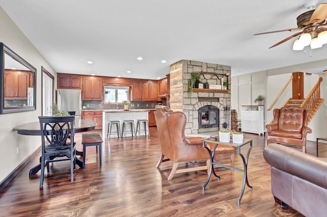 living room featuring a stone fireplace, stairs, a ceiling fan, recessed lighting, and dark wood-type flooring