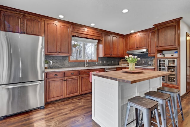 kitchen with appliances with stainless steel finishes, a sink, wine cooler, wood counters, and under cabinet range hood