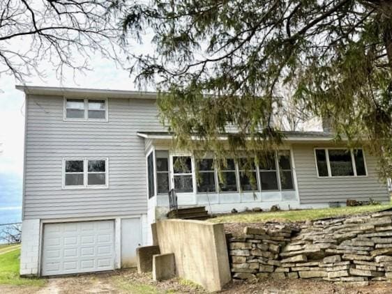 rear view of property featuring dirt driveway, a sunroom, and an attached garage