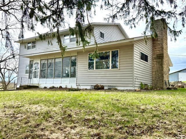 back of property with a sunroom, a yard, and a chimney
