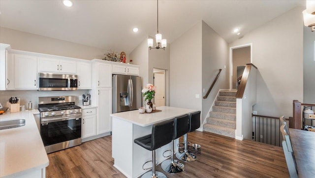 kitchen featuring appliances with stainless steel finishes, wood finished floors, light countertops, white cabinets, and lofted ceiling