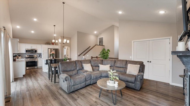 living area with recessed lighting, high vaulted ceiling, an inviting chandelier, and wood finished floors