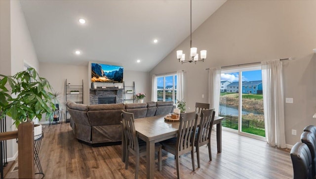 dining space featuring high vaulted ceiling, wood finished floors, a stone fireplace, and a notable chandelier