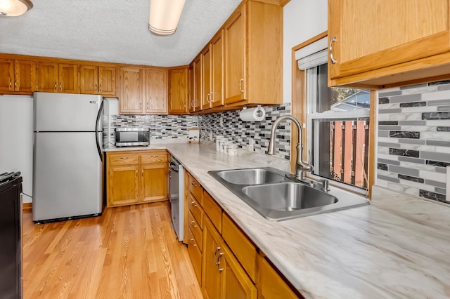 kitchen with appliances with stainless steel finishes, backsplash, light wood finished floors, and a sink
