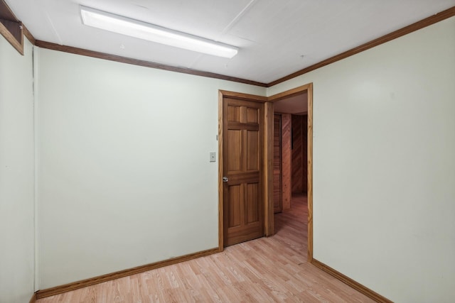 spare room featuring crown molding, light wood-style flooring, and baseboards