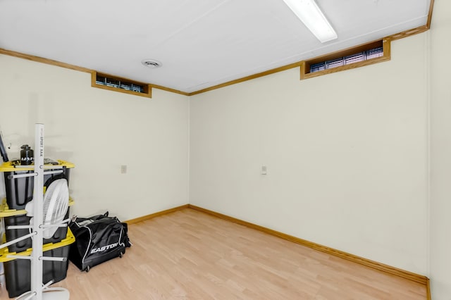 finished below grade area featuring baseboards, ornamental molding, and light wood-style floors