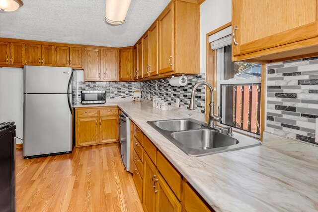 1270 46th Ave NE, Columbia Heights, MN 55421 - kitchen featuring stainless steel appliances, a sink, light wood-type flooring, decorative backsplash, and a textured ceiling