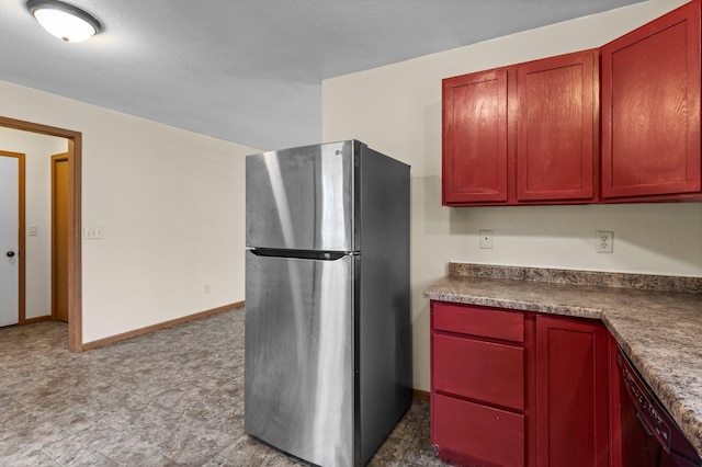 kitchen with dark countertops, reddish brown cabinets, dishwasher, and freestanding refrigerator