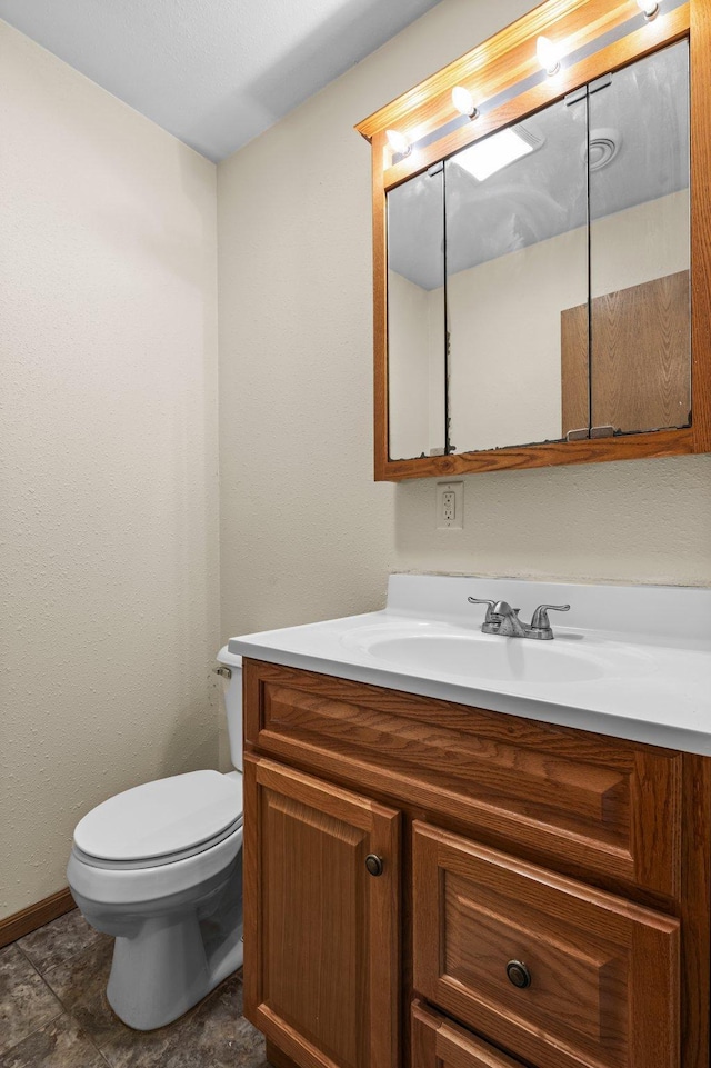 half bath featuring toilet, vanity, and baseboards