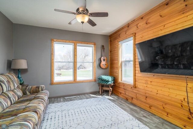 living area featuring wood walls, wood finished floors, ceiling fan, and visible vents