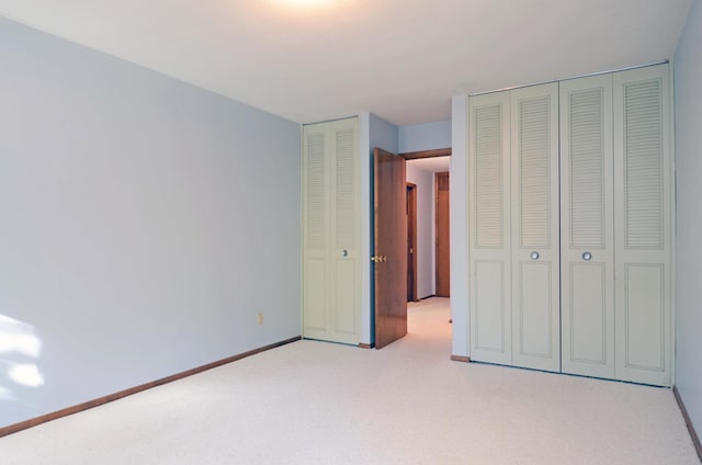 unfurnished bedroom featuring baseboards, two closets, and light colored carpet