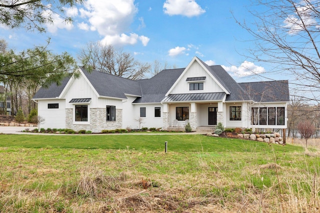 modern farmhouse style home with stone siding, board and batten siding, a front yard, and a standing seam roof
