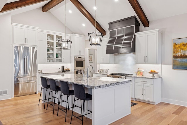 kitchen with stainless steel appliances, wall chimney range hood, a breakfast bar area, light wood-style flooring, and white cabinets