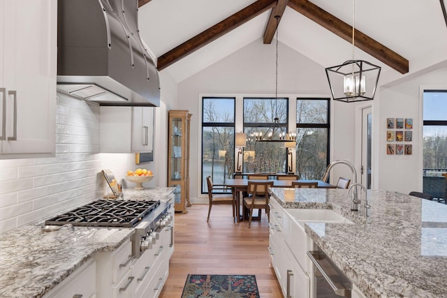 kitchen with an inviting chandelier, a sink, wall chimney exhaust hood, stainless steel appliances, and light wood-type flooring