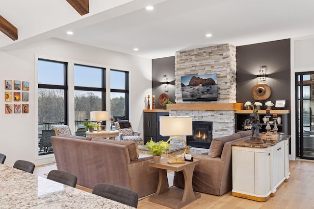 living area with light wood-style floors, beam ceiling, a stone fireplace, and recessed lighting